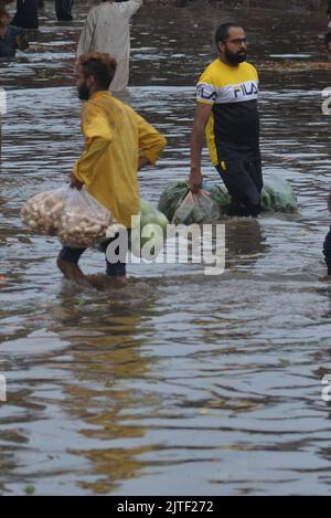 Lahore, Pakistan. 29th Aug, 2022. Pakistani people on their way and busy in Badami bagh vegetable market during heavy monsoon rainfall in Lahore, Pakistan on August 29, 2022. The monsoon rain has broken a 20-year record as the provincial capital received 248mm of downfall in Eight hours. At least Five people are dead and many injured after two roof and walls collapse and other incidents in provincial capital city Lahore. (Photo by Rana Sajid Hussain/Pacific Press/Sipa USA) Credit: Sipa USA/Alamy Live News Stock Photo