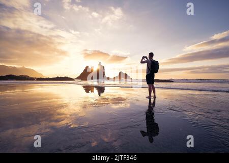 Man during photographing landscape with cliff. Photographer on beach at beautiful sunset. Tenerife, Canary Islands, Spain. Stock Photo