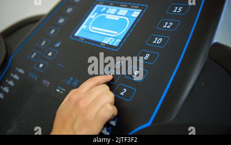 A closeup shot of a female pushing a bottom on a treadmill gym equipment Stock Photo