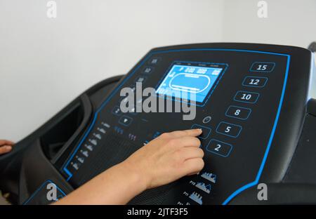 A closeup shot of a female pushing a bottom on a treadmill gym equipment Stock Photo