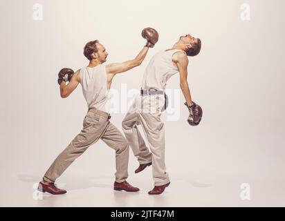 Portrait of two men playing, boxing in gloves isolated over grey studio ...