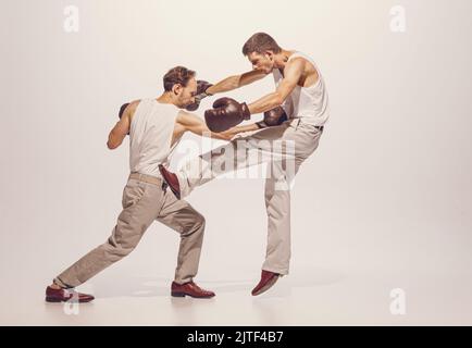 Portrait of two men playing, boxing in gloves isolated over grey studio background. Dynamic image of fight Stock Photo