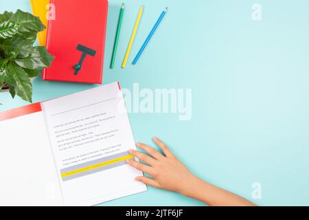 Child affected by dyslexia doing homework, reading book using colored rulers overlays strips. Top view to desk with books and school supplies Stock Photo