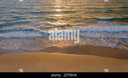 Calm ocean waves rolling onto sandy beach at sunrise Stock Photo