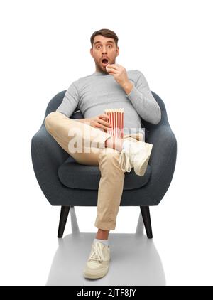 surprised man eating popcorn sitting in chair Stock Photo