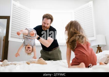 Father playing with son (12-17 months) and daughter (2-3) on bed Stock Photo