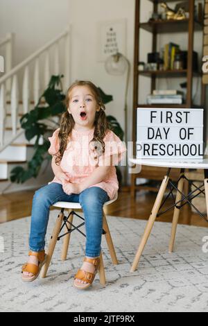 Portrait of girl (2-3) making faces at First day of preschool sign Stock Photo