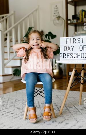 Portrait of girl (2-3) making faces at First day of preschool sign Stock Photo