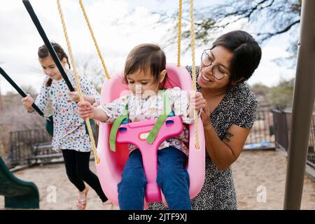 Mother with daughters (2-3, 8-9) on playground swings Stock Photo