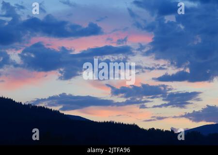 Pink glow on high clouds after sunset with foreground tree line in shadow Stock Photo