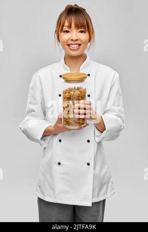 smiling female chef holding jar with pasta
