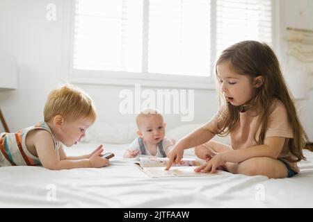 Siblings (6-11 months, 2-3) reading and using phone Stock Photo