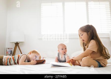 Siblings (6-11 months, 2-3) reading and using phone Stock Photo