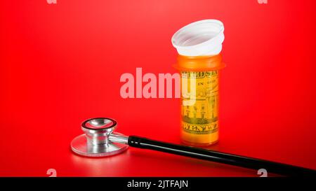Stethoscope with plastic container for pills with dollar cash inside on red background with copy space Stock Photo