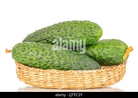 Three organic green cucumbers in a straw bowl, close-up, isolated on a white background. Stock Photo