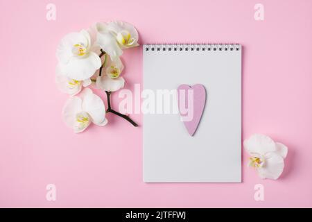 Creative workspace. Notepad sheet and white orchid flowers on a pink background. Stock Photo
