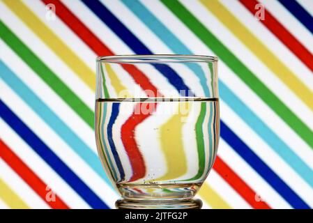 Ilusión óptica creada mediante la refracción de la luz con un vaso de agua y lineas diagonales de colores Stock Photo