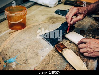 Unrecognizable person making handmade ax. Closeup old senior male hand creating wooden handle for axe. Mature man working in carpentry workshop concep Stock Photo