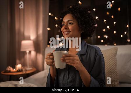 happy woman with coffee sitting in bed at night Stock Photo