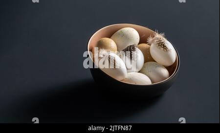 easter eggs with feathers in bowl on black table Stock Photo