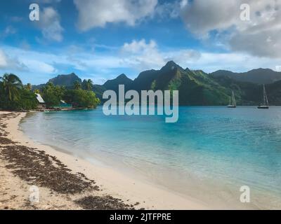 Tropical island beach, Moorea, French Polynesia. Crystal water sea bay, white sand beach, green mountain range in background. Virgin untouched nature sea lagoon, yacht tour, exotic travel destination Stock Photo