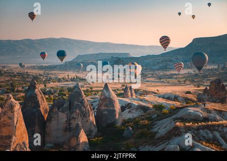 Cappadocia aerial sunrise landscape, colorful hot air balloons fly over cave house and famous fairy chimneys in Goreme national park. People enjoy wonderful aerial sun rise watching. Travel background Stock Photo