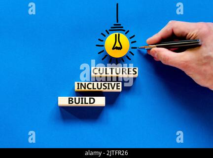 Build inclusive cultures symbol. Concept words Build inclusive cultures on wooden blocks. Businessman hand. Beautiful blue background. Business build Stock Photo