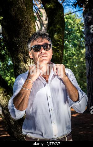 The young man is wearing sunglasses and is walking in the park. The handsome businessman is working outdoors. Stock Photo