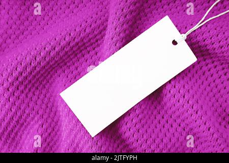 White blank rectangular clothing tag, label mockup template on purple knitted fabric background . Price tag label with copy space for text. Shopping, Stock Photo
