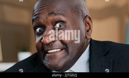 Close up front view male wrinkled elderly face emotional funny frightened puzzled African business man looking at camera feeling shock fright disgust Stock Photo