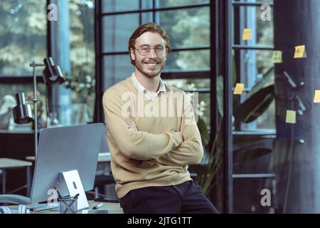 Portrait of successful young IT specialist young engineer programmer in modern loft office smiling and looking camera with crossed arms, businessman business owner wearing glasses and casual clothes Stock Photo