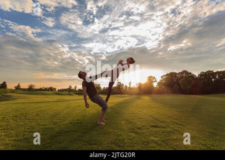 Healthy young man holds in the air a woman balancing and doing acro yoga Stock Photo