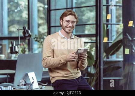Portrait of young businessman businessman man blond smiling and looking at camera, at work in modern loft office, using tablet computer, IT specialist testing new software application Stock Photo