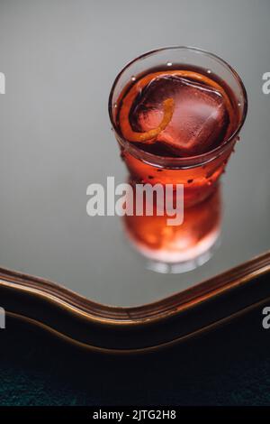 red negroni cocktail with piece of orange and large ice cube in glass on mirror Stock Photo