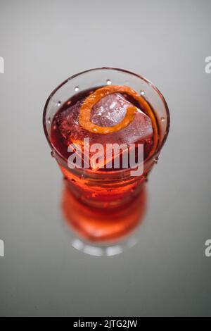 red negroni cocktail with piece of orange and large ice cube in glass on gray background Stock Photo
