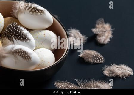easter eggs with feathers in bowl on black table Stock Photo