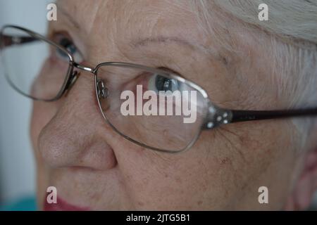 Close up portrait of beautiful older woman smiling and standing by wall with gray eyes. Stock Photo