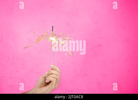 hand with sparkler burning over pink background Stock Photo