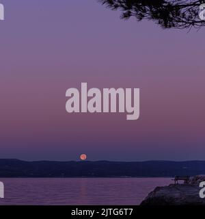 A beautiful view of the setting moon and the island at dawn on the coast of the Adriatic Sea in Croatia. Concept summer vacation. Stock Photo