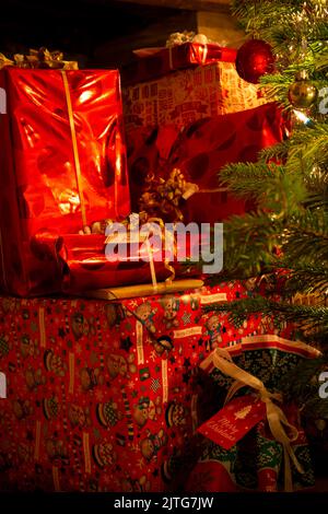 A warm glow over a Pile of Christmas gifts presents alongside a Christmas tree Stock Photo