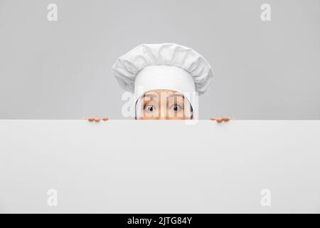 female chef peeking out from behind white board Stock Photo