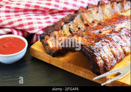 grilled pork ribs on a wooden cutting board with kitchen fork for meat and tomato ketchup Stock Photo