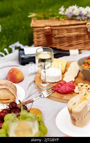 food, drinks and picnic basket on blanket on grass Stock Photo