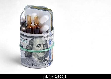 Tablets and ampoules in a blister pack are wrapped in hundred dollar bills, fastened with an elastic band, isolated on a white background Stock Photo