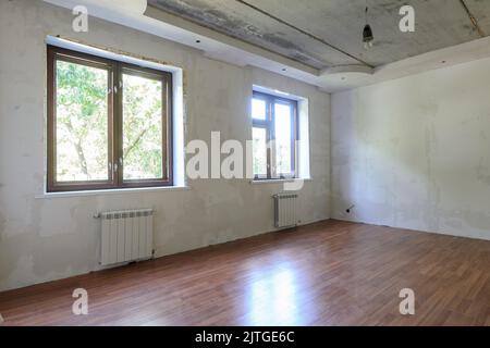 The interior of an empty room during renovation, there are two large windows in the room, heating radiators are located under the windows Stock Photo