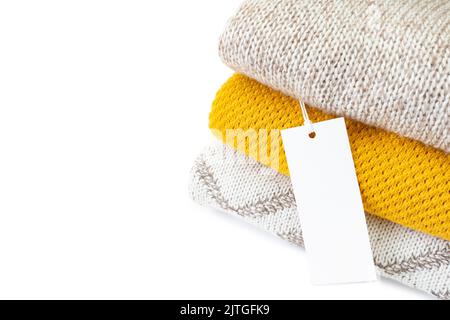 White blank rectangular clothing tag, label mockup template on heap of knitted clothes isolated on white background . Price tag label with copy space Stock Photo