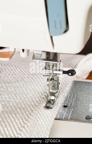 Professional equipment. Modern sewing machine with special pressure foot. The process of sewing a decorative edging cord of white item of clothing. Stock Photo