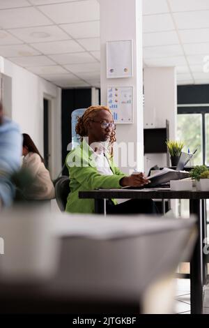 Employee working with business documents, analyzing financial report in office open space, woman sitting at workplace desk. Young woman looking at company papers, side view Stock Photo