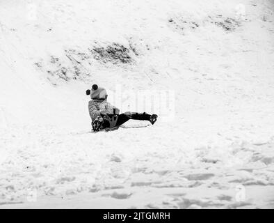 Dnepropetrovsk, Ukraine - 12.31.2021: Little girl sledding down a slide in winter. Outdoor play for children. Childhood, leisure and season concept. Stock Photo