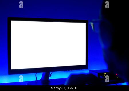 close-up side view of man watching a computer monitor in the dark, with blue led lights around it, in a home music studio, with focus on the screen. Stock Photo